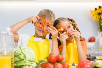 Happy kids having fun with food vegetables at kitchen holds pepper before his eyes like in glasses